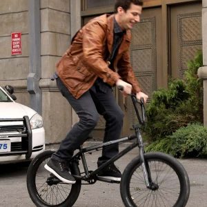 Actor Andy Samberg riding a bicycle he Wearing Brown Leather Jacket In TV Series Brooklyn Nine-Nine as Jake Peralta